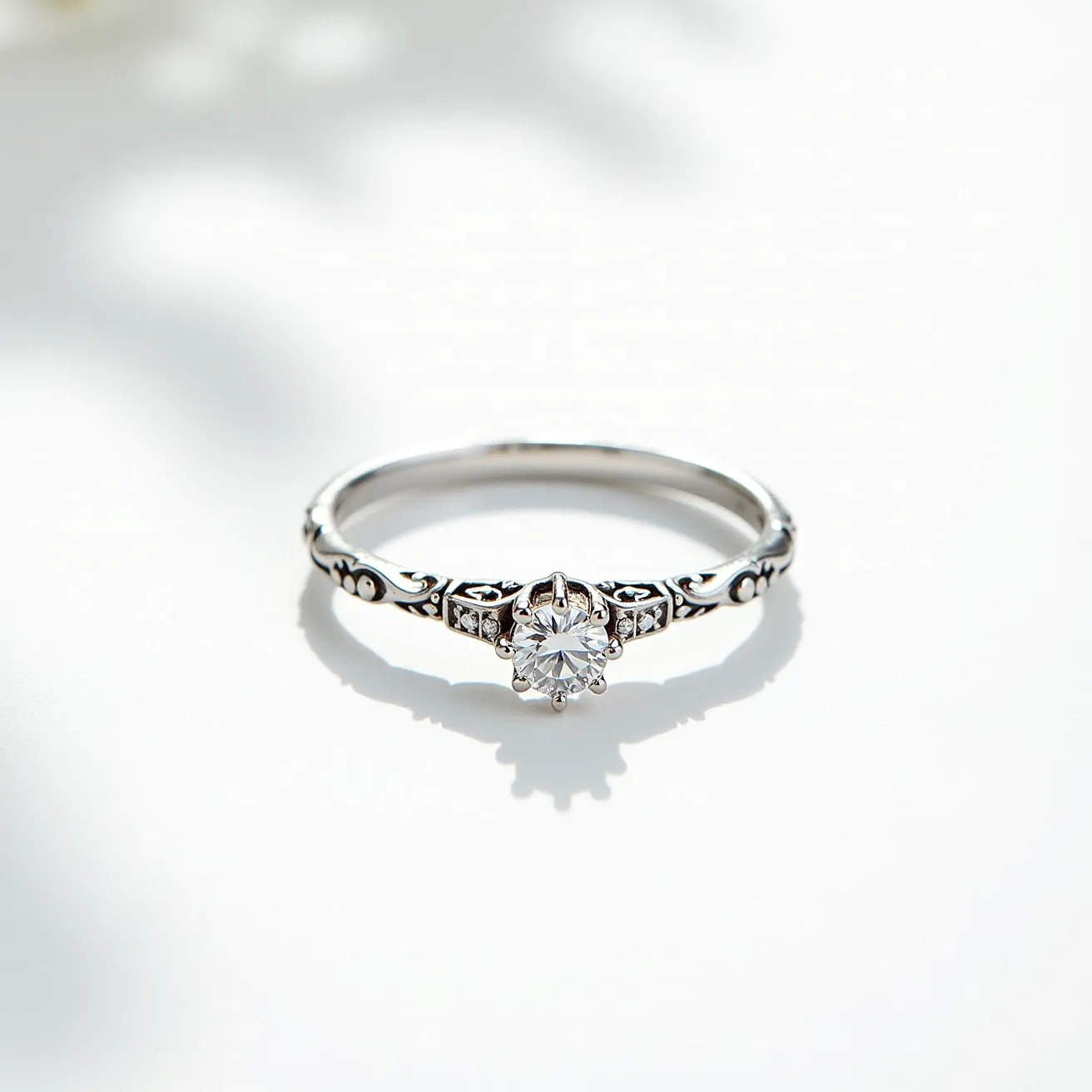 This wedding ring features a delicate and intricate design crafted from a shiny metal, likely white gold or platinum. The focal point of the ring is a round cut gemstone, possibly a diamond, set in a classic prong setting that elevates the stone to catch the light. The band is adorned with elegant filigree work and small accent stones that add sophistication and detail, enhancing the overall vintage aesthetic of the ring. The combination of the central gemstone, accent stones, and the ornate metalwork creates a timeless and elegant piece suitable for a special occasion.