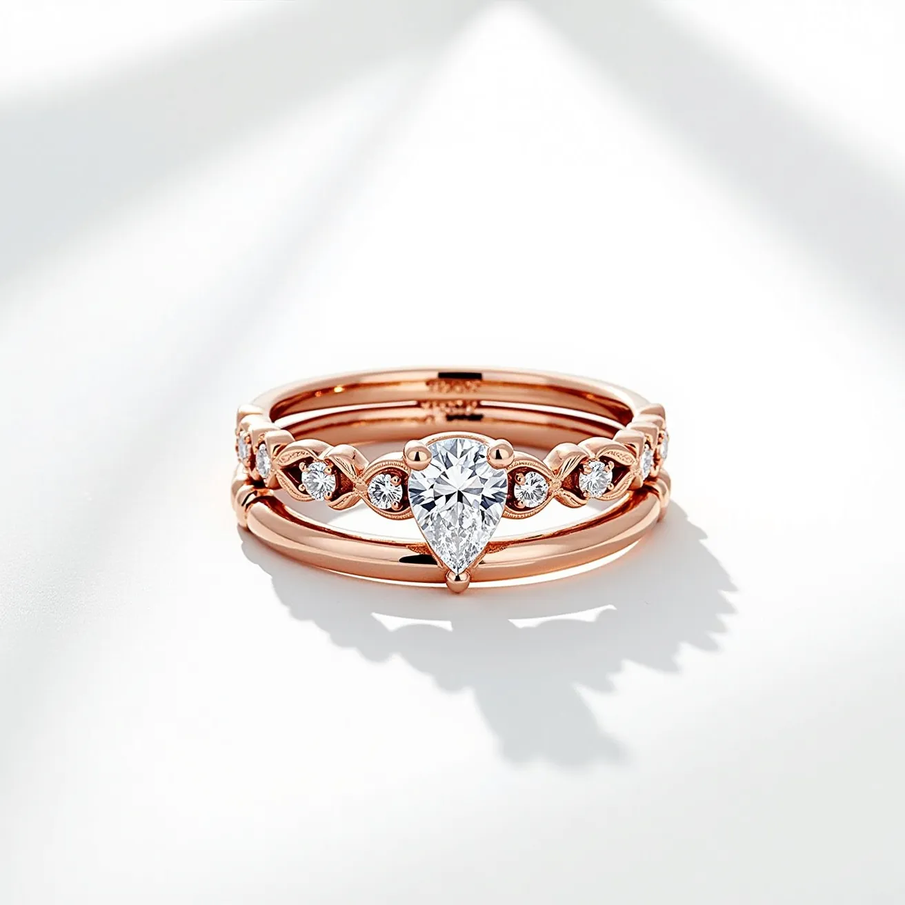 This wedding ring set is crafted with a warm rose gold band, elegantly adorned with a series of diamonds. The central gemstone is a pear-shaped diamond, prominently set in a prong setting that enhances its brilliance and prominence. Flanking the centerpiece are additional round-cut diamonds, each nestled in their own delicate prong settings, adding to the ring's overall sparkle and allure. The intricate design and choice of precious materials make this set a symbol of timeless elegance and romance.