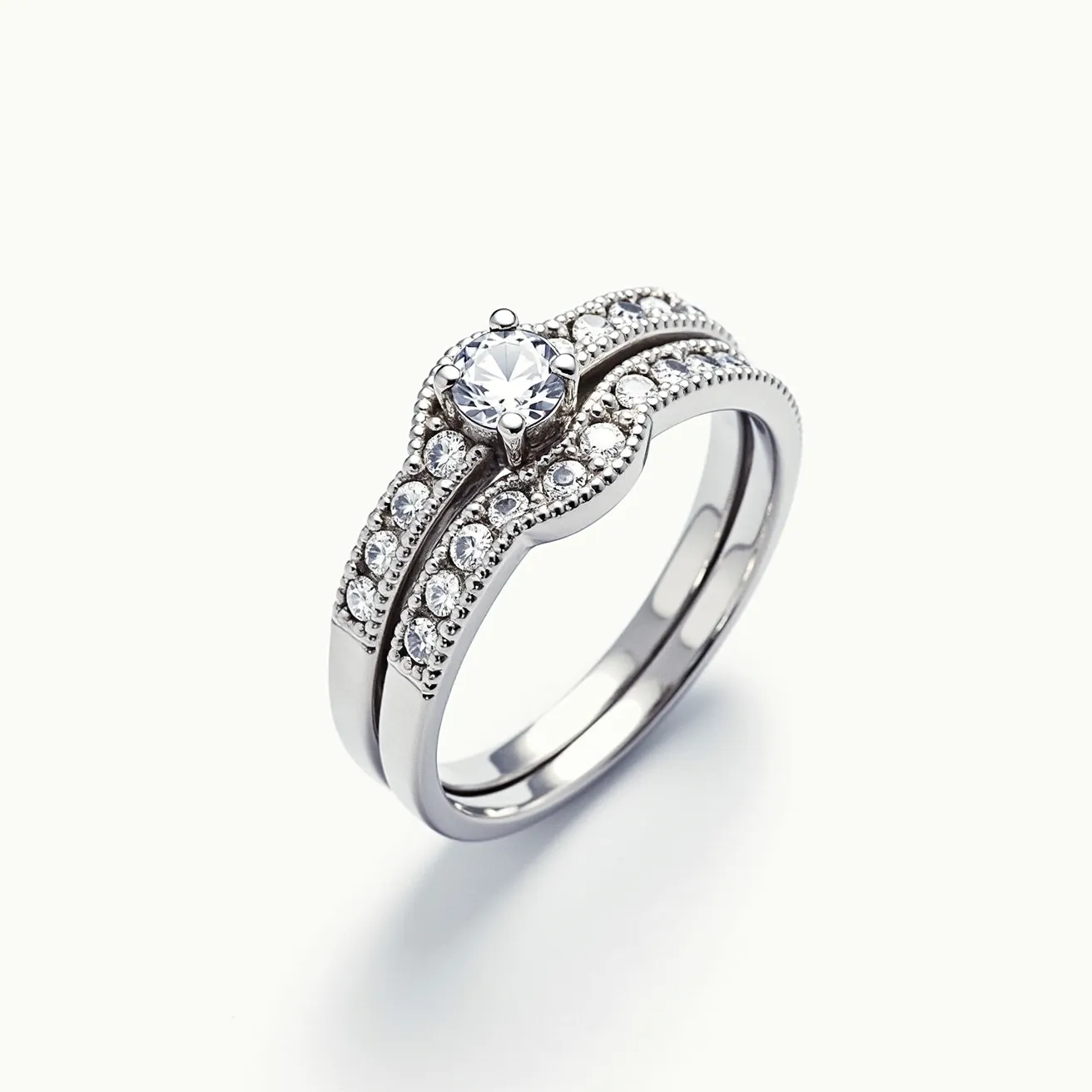 This wedding ring set features a stunning ensemble crafted from a lustrous metal, likely white gold or platinum. The centerpiece of the engagement ring is a brilliant round-cut gemstone, secured in a classic prong setting, enhancing its sparkle and prominence. Surrounding the central gem, smaller round stones are intricately embedded in a pave setting along the band, contributing to an elegant and cohesive design. The matching wedding band mirrors this refined aesthetic, with similar small gems set into the band, creating a harmonious and luxurious look. The seamless blend of these elements highlights the meticulous craftsmanship and timeless elegance of the set.