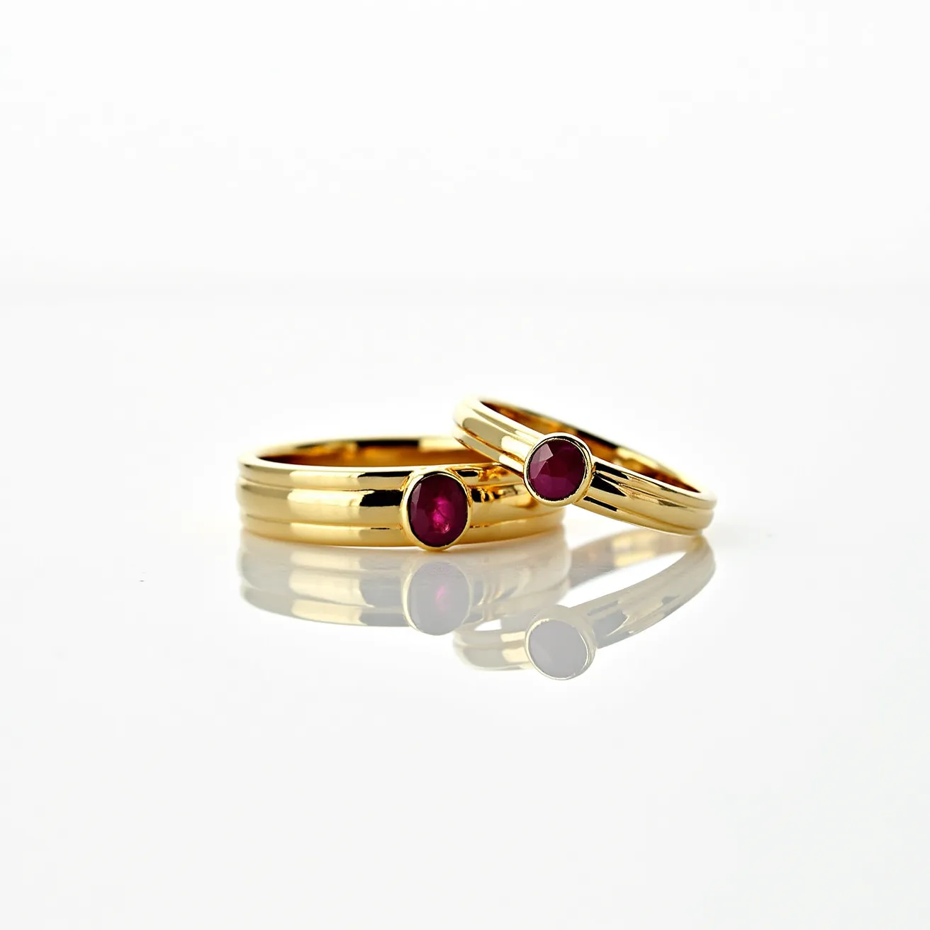 These wedding ring sets are crafted from polished gold, showcasing a classic and elegant design. Each ring features a ruby gemstone, with a smooth round cut, set prominently in a bezel setting. The rich red hue of the rubies contrasts beautifully against the warm yellow tone of the gold bands, creating a harmonious and luxurious look. The rings display a sleek and smooth finish, highlighting their refined craftsmanship.