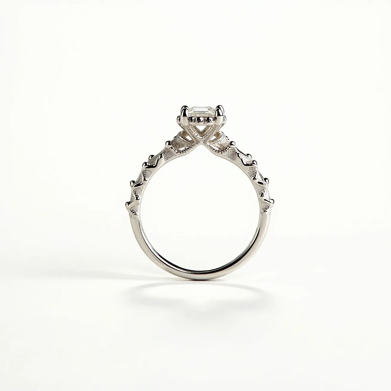 This unique wedding ring is crafted from a polished metal that appears to be white gold or platinum, featuring an intricate and artistic band design with a series of raised, textured accents that give it a modern and elegant appearance. At the center, it showcases a prominent rectangular-cut diamond set within a four-prong mounting, which elevates the gem above the band and allows for maximum light reflection, enhancing its brilliance. The setting seamlessly integrates with the band in a way that complements the overall design, and the craftsmanship highlights both the durability and aesthetic appeal of the piece.