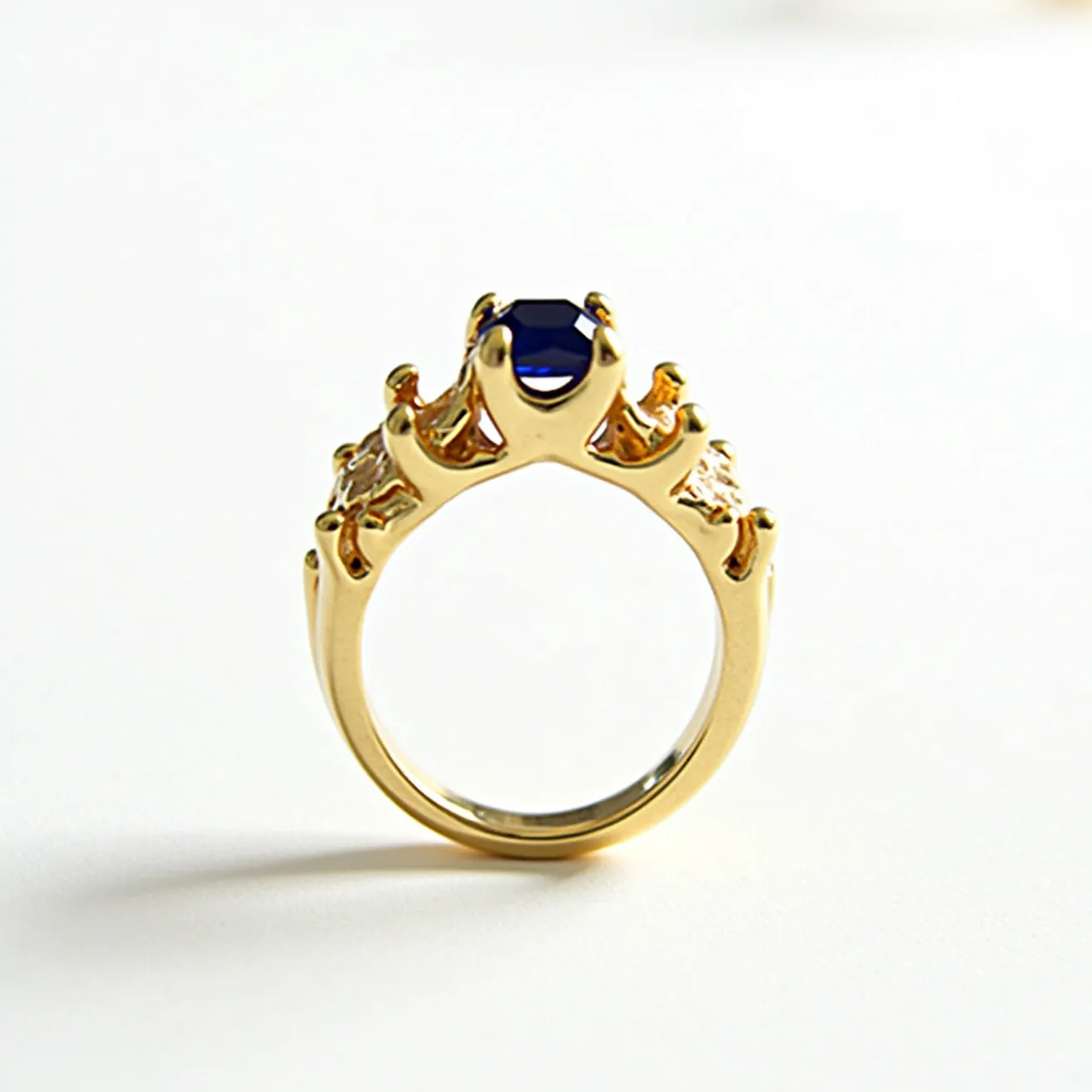 This unique wedding ring is crafted from gold, featuring a striking design that resembles a crown. The focal point of the ring is a captivating blue gemstone, possibly a sapphire, set prominently at the top in a prong setting. The regal design is complemented by smaller accent diamonds or similar stones set along the sides, enhancing the overall elegance of the ring. The craftsmanship combines intricate detailing with a bold aesthetic, making it a standout piece for any wearer.