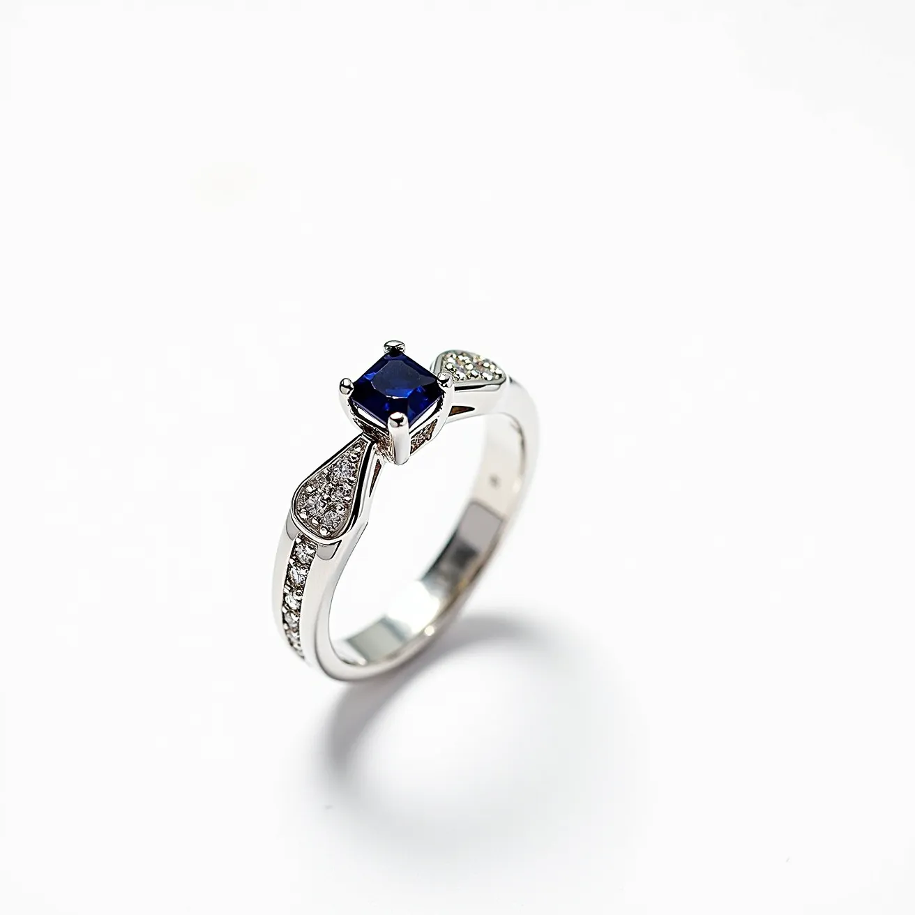 This unique wedding ring showcases a striking design featuring a square-cut blue sapphire as its central gem, securely held by a four-prong setting. Flanking the sapphire, the ring's band is elegantly adorned with small, round brilliant-cut diamonds that enhance its sophisticated look. The band is crafted from a polished white metal, likely white gold or platinum, contributing to its sleek and modern appeal. Delicate pavé diamond accents further embellish the band, adding a touch of sparkle and elegance to this exquisite piece of jewelry.