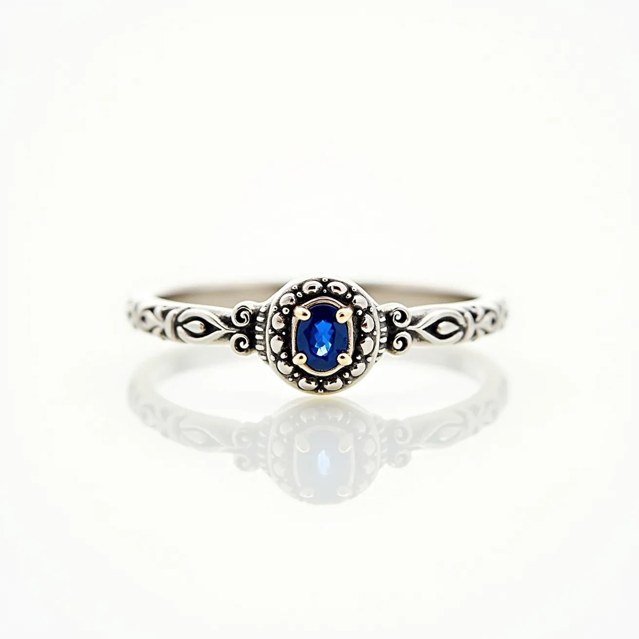 This western wedding ring is crafted from silver with intricate etched designs along its band. The focal point is a striking oval-cut blue sapphire gemstone set in the center, held securely by four prongs. The setting is further adorned with detailed bead-like patterns surrounding the stone, adding an elegant and vintage touch to the overall design.