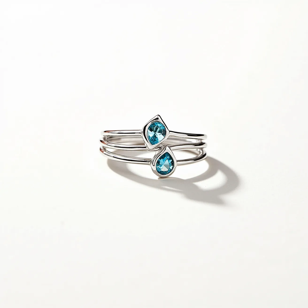 This wrap ring features a sleek, silver band that delicately coils, showcasing a stylish design. It is adorned with two striking blue pear-shaped gemstones, each set in a bezel setting that complements the fluidity of the ring's form. The stones' vibrant color adds a touch of elegance, enhancing the ring's overall aesthetic appeal and versatility.