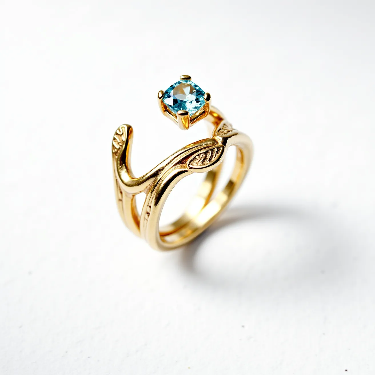 This wrap ring features a design reminiscent of natural vines and leaves, crafted from a gold-toned metal. A single blue gemstone, possibly a topaz, sits prominently in a prong setting at the top of the ring, showcasing a round cut that enhances its brilliance. The detailed vine design integrates seamlessly with the gemstone, adding an organic aesthetic to the piece. The ring's band spirals gracefully, with intricate leaf motifs enhancing its elegance and making it a striking accessory.