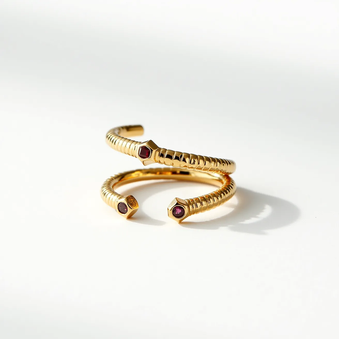 This wrap ring features a gold-toned, flexible band that spirals elegantly. Its design incorporates hexagonal settings on two ends, each housing a small, deep red stone, possibly a garnet, with a flat, polished cut. The stones are securely set, flush with the surface of the metal. This construction gives the ring a seamless, continuous appearance, enhancing its sophisticated and modern aesthetic. 