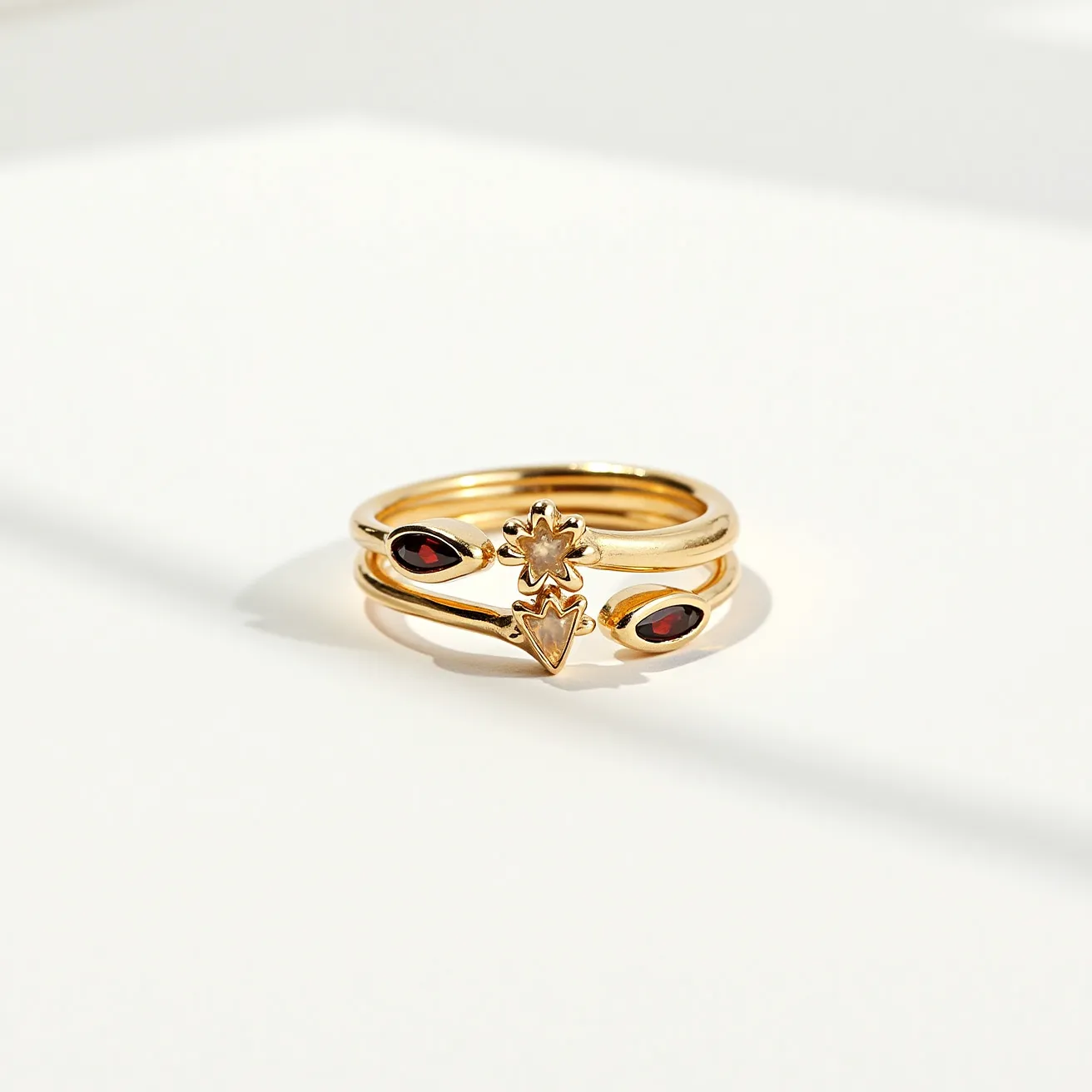 This wrap ring elegantly combines delicate gold bands with distinctive design elements, featuring two marquise-cut red gemstones set horizontally on either side of a central motif. The gold bands twist and overlap, forming a visually complex and appealing structure. At the center of the ring, a decorative floral pattern enhances the overall charm, its petals shining with the same golden material. The absence of clasps indicates a continuous wrap design, ensuring both style and comfort for the wearer.